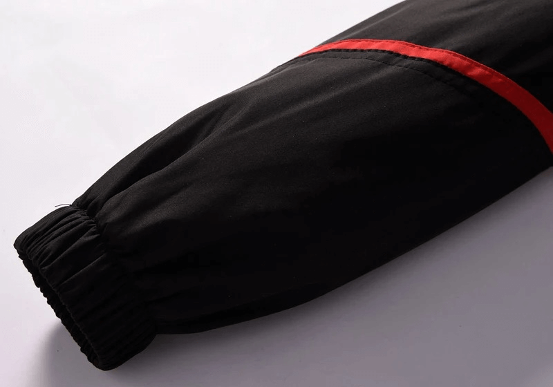 Close-up of black athletic jacket sleeve with red stripe, featuring an elastic cuff for a snug fit.